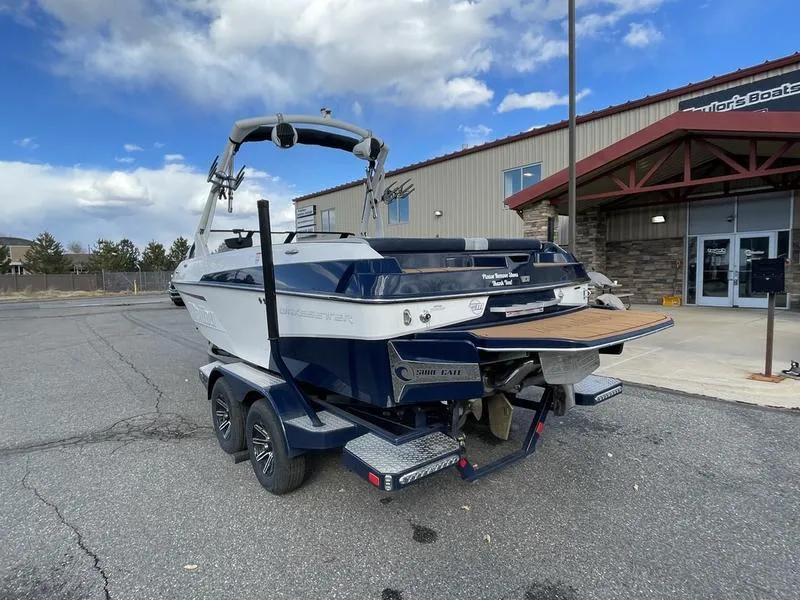 Slide: The Image of 2025 Malibu 20 VTX boat on trailer, parked outside a building under a blue sky. - 9