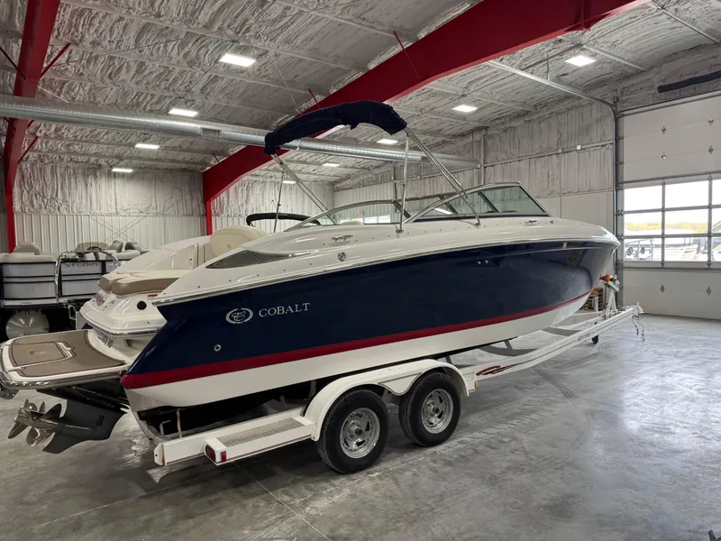 Slide: The Image of 2012 Cobalt 262 BR boat in a warehouse, on a trailer, with a blue and white exterior. - 3