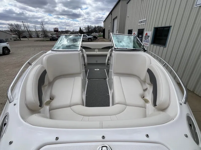 Slide: The Image of 2004 Chaparral 210 SSi boat with white seating, docked near a metal building. - 3