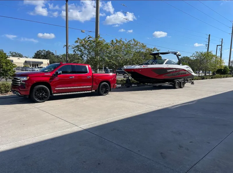 Slide: The Image of Red truck towing a 2023 Scarab 285 ID boat on a sunny day. - 2