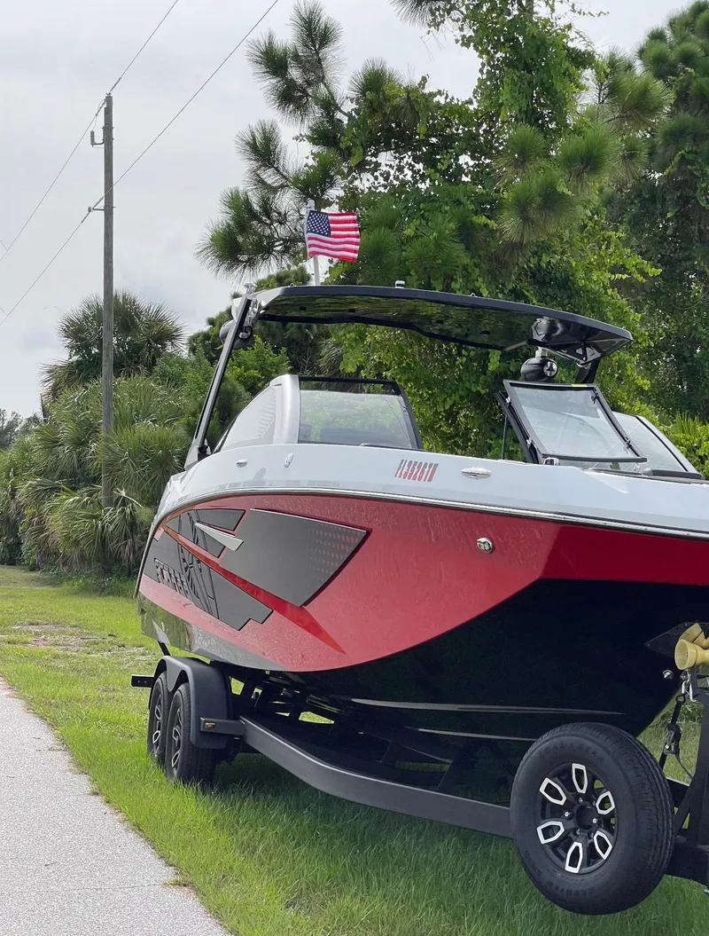 Slide: The Image of 2023 Scarab 285 ID boat on trailer, red and black design, parked roadside with American flag. - 3