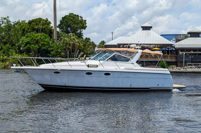 The Image of 2000 Tiara Yachts 3500 Express cruising on a calm river near a waterfront building. - 0
