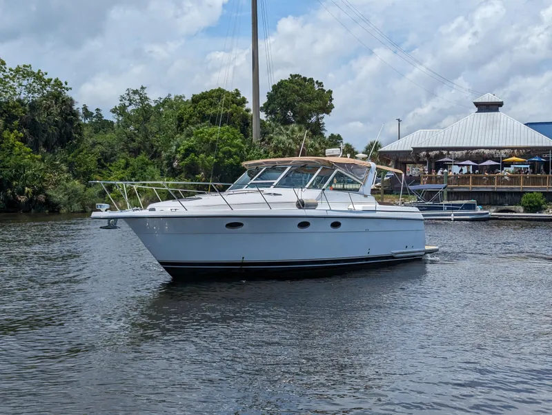 Slide: The Image of 2000 Tiara Yachts 3500 Express cruising on a calm river near a dockside restaurant. - 34