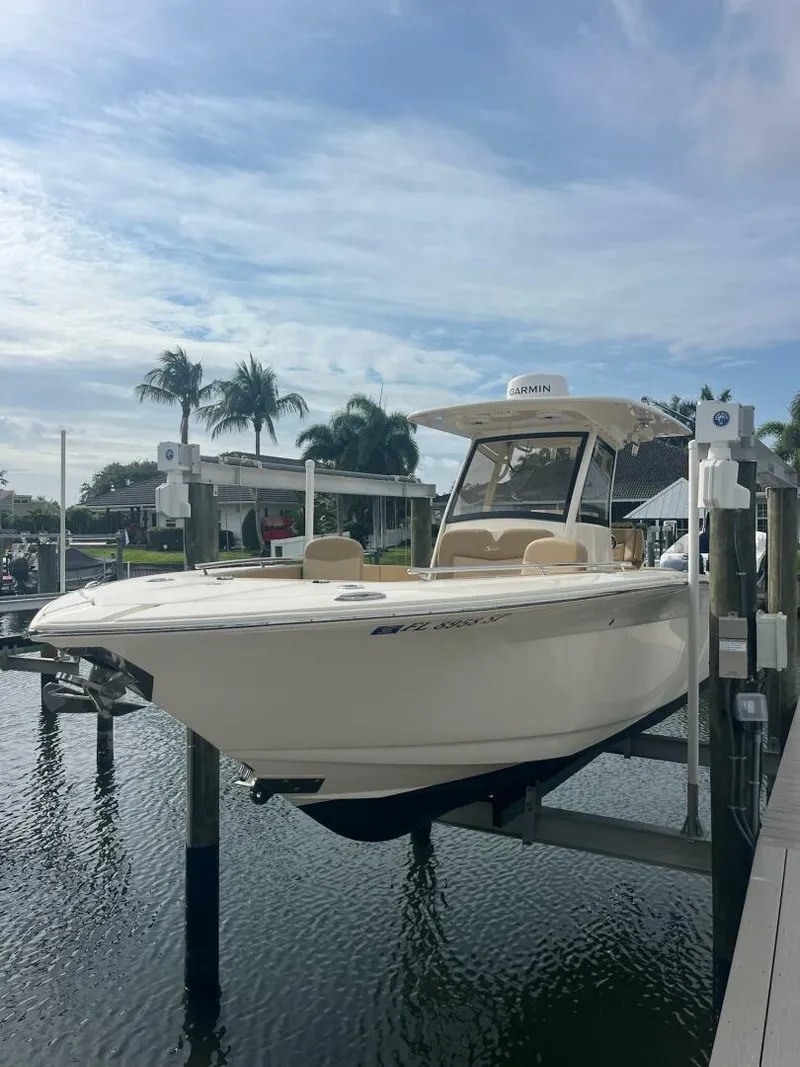 Slide: The Image of 2020 Scout 277LXF boat docked on lift, surrounded by water and palm trees. - 1