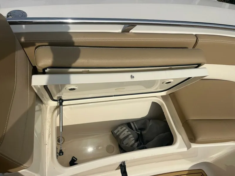 Slide: The Image of 2020 Scout 277LXF boat storage compartment with open lid and beige seating. - 13