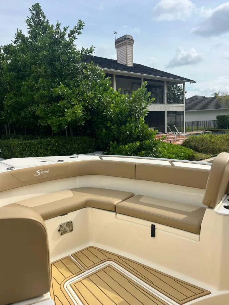 Slide: The Image of 2020 Scout 277LXF boat with tan seating, wooden deck, and house in the background. - 8