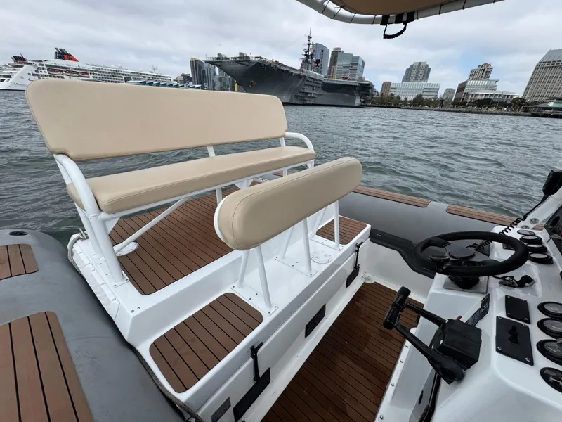 Slide: The Image of Nautica 33 Commercial RIB, 1995, with beige seating, on water near cityscape and ships. - 2