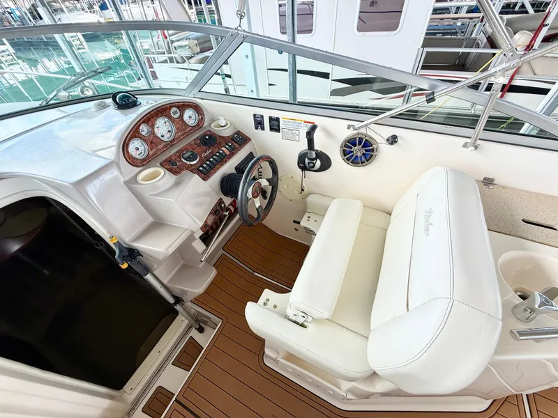 Slide: The Image of 2006 Rinker 270 Express Cruiser helm with white seating and wood-accented dashboard. - 5