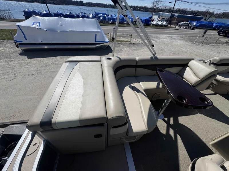 Slide: The Image of 2015 Bennington 20 SL pontoon boat with beige seating and a wooden table, near a waterfront. - 10