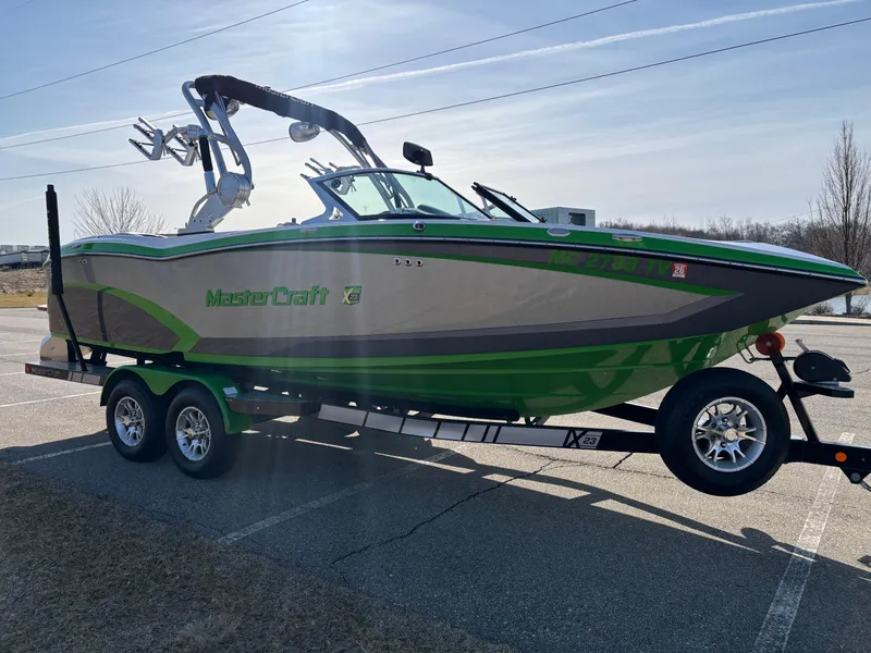 Slide: The Image of 2015 MasterCraft X23 boat on trailer, green and gray design, parked in a lot. - 21