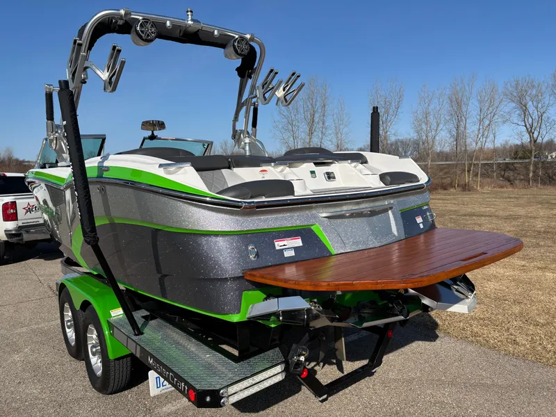 Slide: The Image of 2015 MasterCraft X23 boat with green accents on a trailer, parked outdoors. - 4