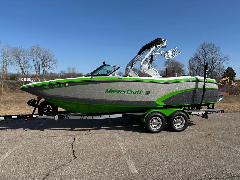 Slide: The Image of 2015 MasterCraft X23 boat in green and gray on a trailer, parked outdoors. - 5
