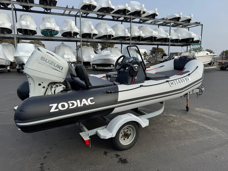 Slide: The Image of 2023 Zodiac Open 4.2 boat with Suzuki engine on a trailer, parked in a marina. - 4