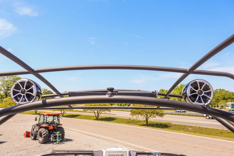 Slide: The Image of 2024 Yamaha Boats 255XD wakeboard tower with speakers, parked near a road and tractor. - 27