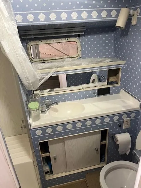 Slide: The Image of 1970 Chris-Craft Commander Sport Cruiser bathroom with blue seashell wallpaper and compact fixtures. - 16