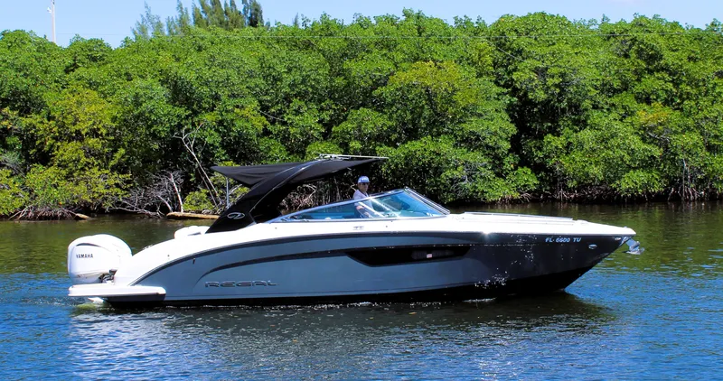 Slide: The Image of 2022 Regal 33 OBX boat cruising on a calm river with lush green trees in the background. - 0