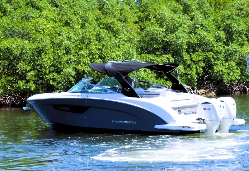 Slide: The Image of 2022 Regal 33 OBX boat cruising on a sunny day near lush greenery. - 6