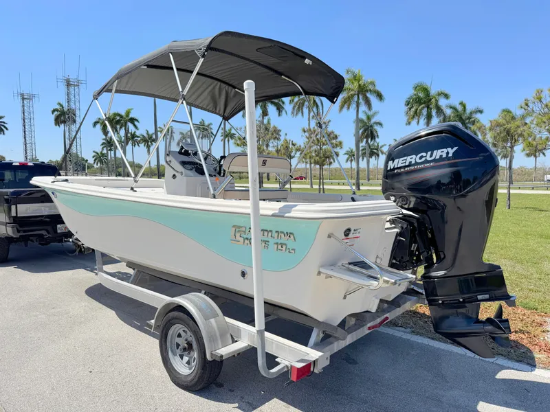 Slide: The Image of 2020 Carolina Skiff 19 LS boat on trailer with Mercury outboard motor, parked near palm trees. - 2