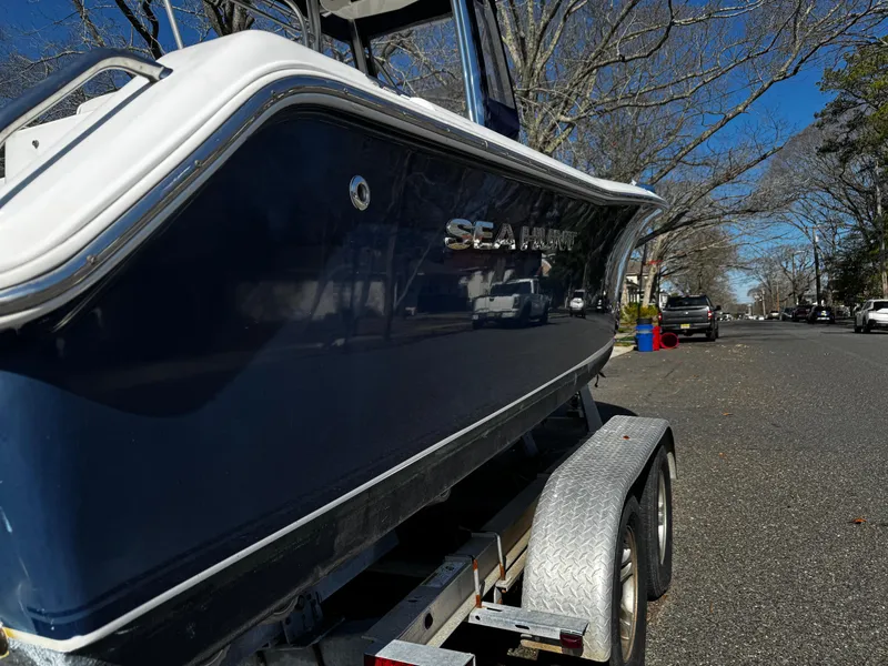 Slide: The Image of 2012 Sea Hunt Triton 210 boat on trailer, parked on a tree-lined street. - 2