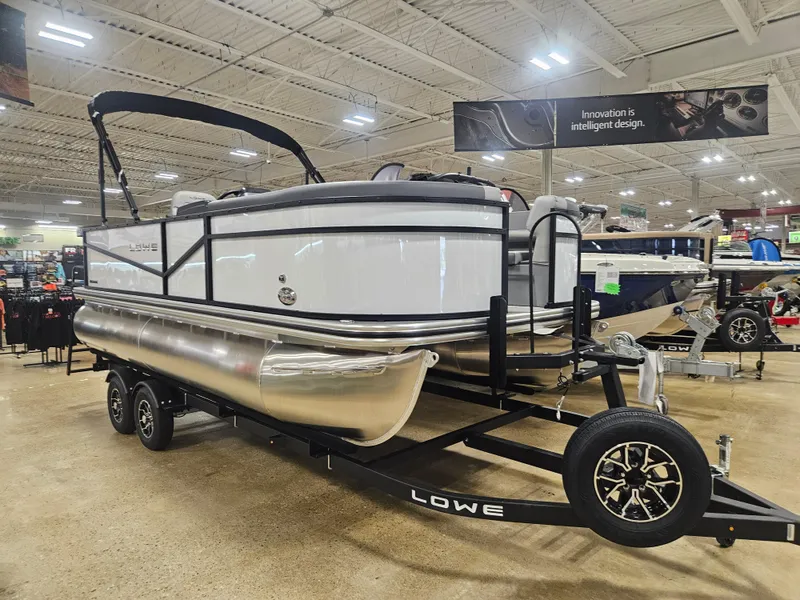 Slide: The Image of 2025 Lowe LS190 pontoon boat displayed indoors on a trailer. - 0