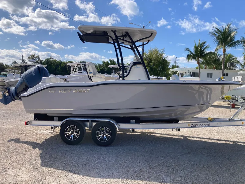 Slide: The Image of 2025 Key West 219fs boat on trailer under blue sky with palm trees. - 2