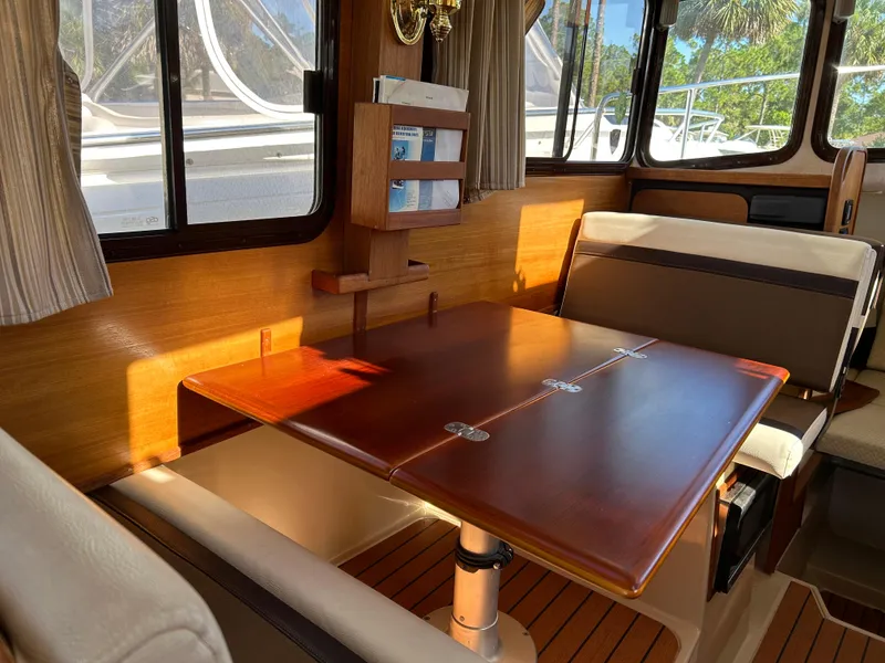 Slide: The Image of 2017 Ranger Tugs R-27 interior with wooden table and seating, sunlight streaming through windows. - 24