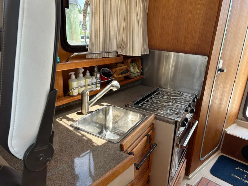 Slide: The Image of 2017 Ranger Tugs R-27 boat kitchen with sink, stove, and wooden cabinetry. - 25