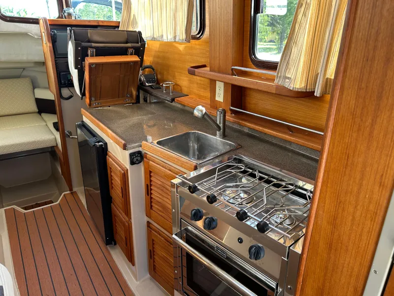 Slide: The Image of 2017 Ranger Tugs R-27 boat interior with kitchen, stove, sink, and wooden cabinetry. - 27