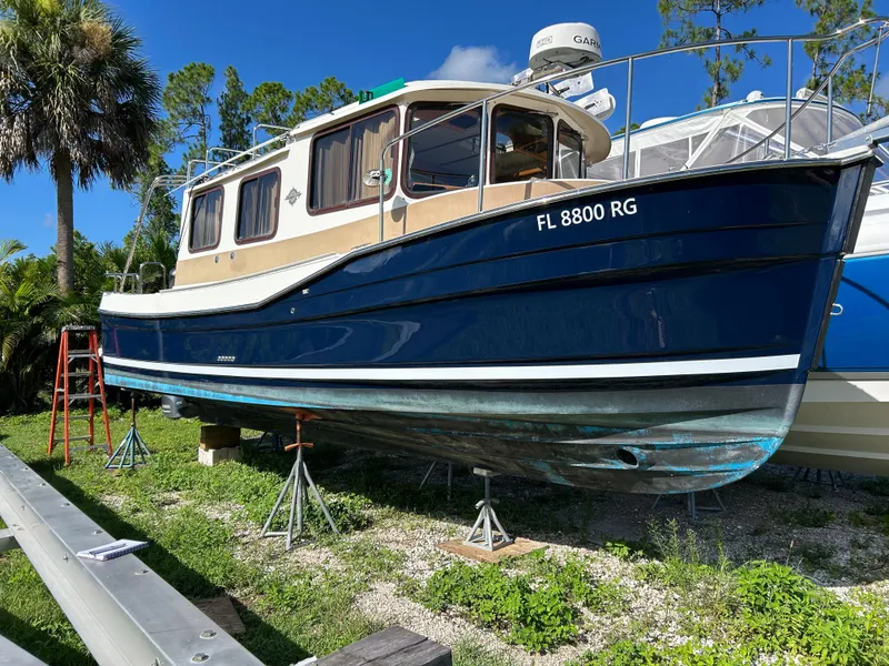 Slide: The Image of 2017 Ranger Tugs R-27 boat on stands, blue hull, sunny day, palm trees in background. - 6