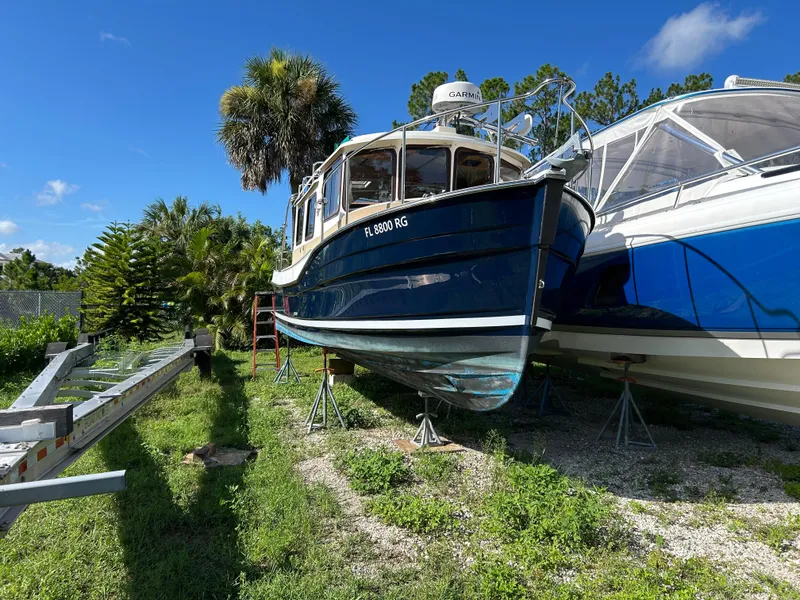 Slide: The Image of 2017 Ranger Tugs R-27 boat on stands, surrounded by greenery and clear blue sky. - 7