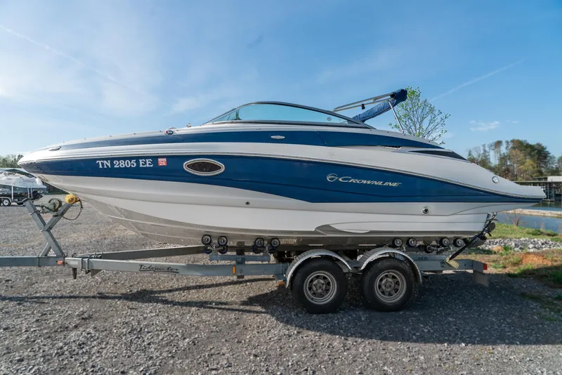Slide: The Image of 2012 Crownline Eclipse E2 boat on trailer, blue and white design, parked outdoors. - 2