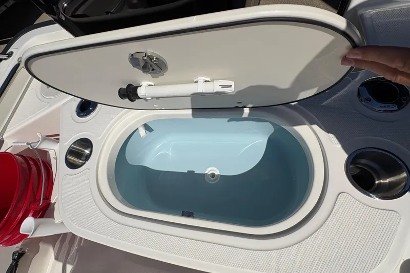 Slide: The Image of Open storage compartment on 2026 Boston Whaler 150 Montauk boat, featuring cup holders and a red bucket. - 7