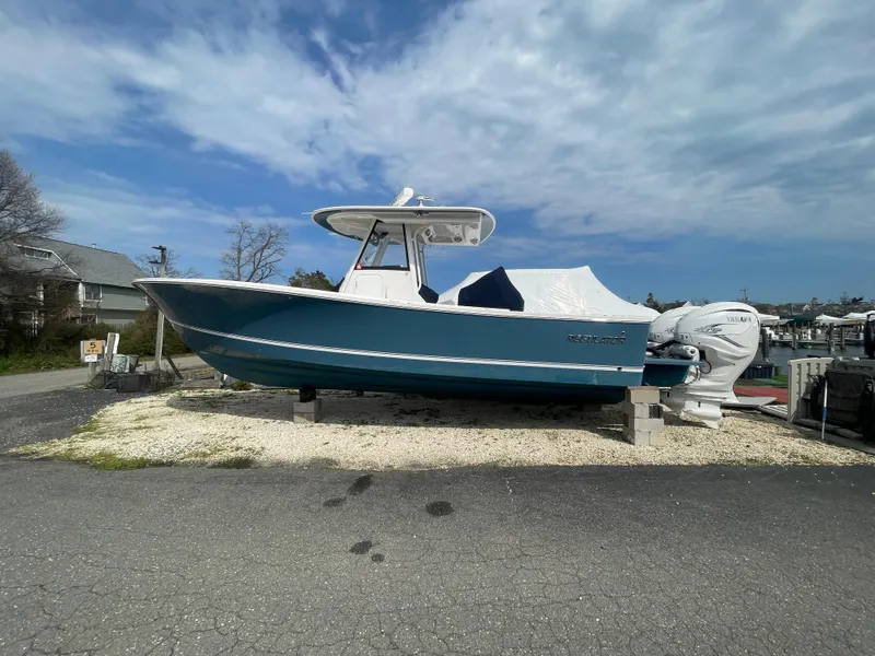 Slide: The Image of 2022 Regulator 31 boat on display, blue hull, covered, parked on gravel. - 3