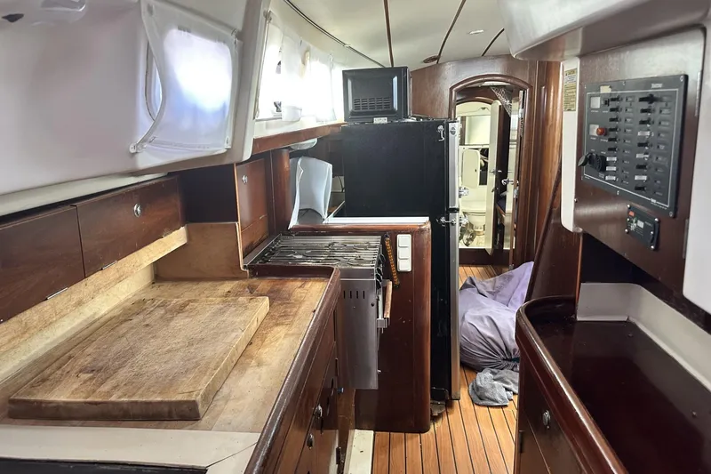 Slide: The Image of Interior of 1999 Beneteau Oceanis 400 yacht, featuring a compact kitchen and wooden cabinetry. - 12