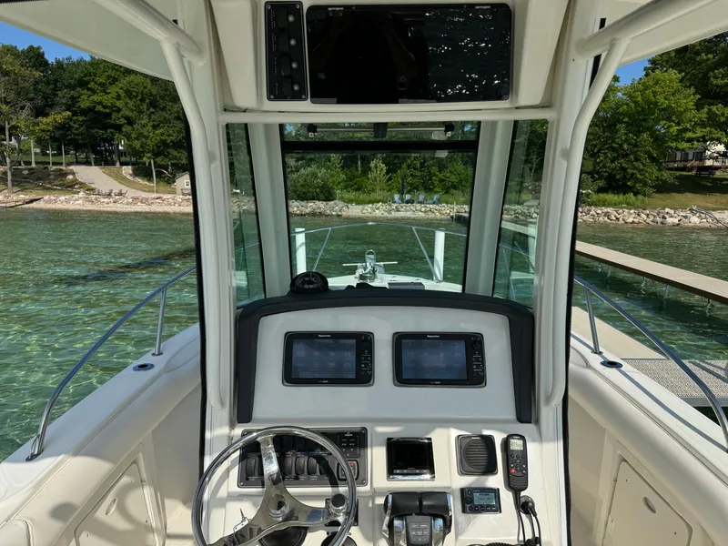 Slide: The Image of 2015 Boston Whaler 250 Outrage helm with dual displays, steering wheel, and clear water view. - 15