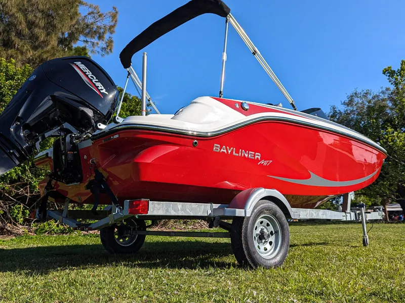 Slide: The Image of 2025 Bayliner Element M17 boat on trailer, vibrant red hull, parked on grass. - 1