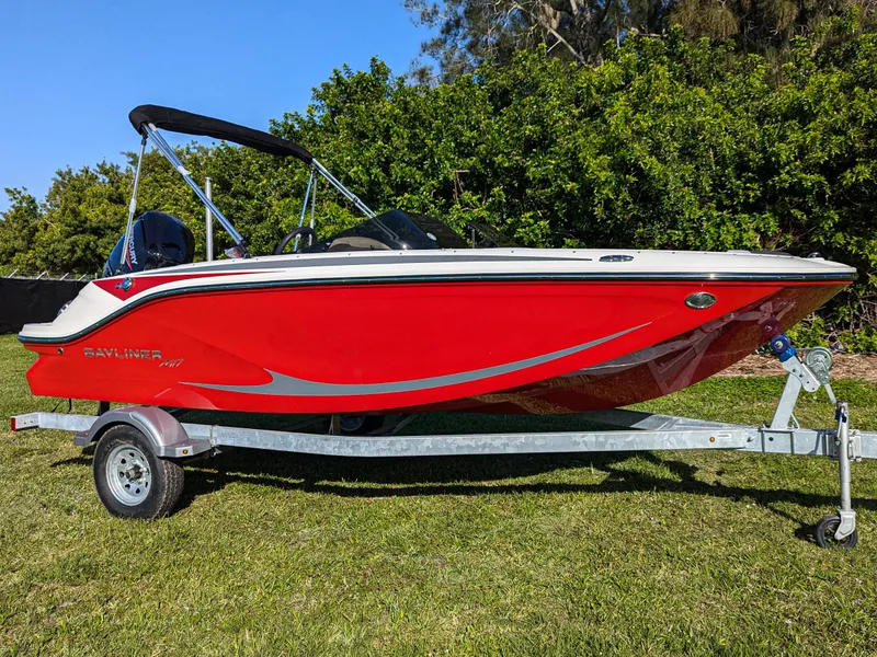 Slide: The Image of 2025 Bayliner Element M17 boat in vibrant red on a trailer, parked on grass. - 4