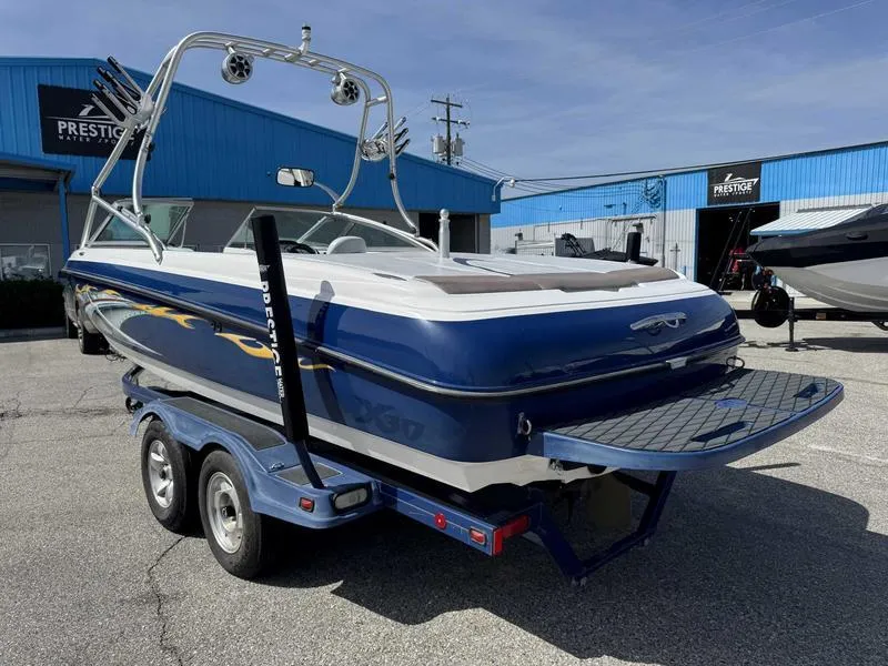 Slide: The Image of 2004 MasterCraft X30 boat on trailer, blue and white, parked near blue buildings. - 5