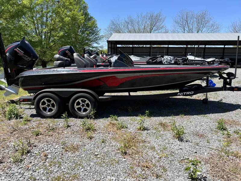 The Image of 2024 Nitro Z19 boat on trailer, parked outdoors, surrounded by greenery and gravel. - 1