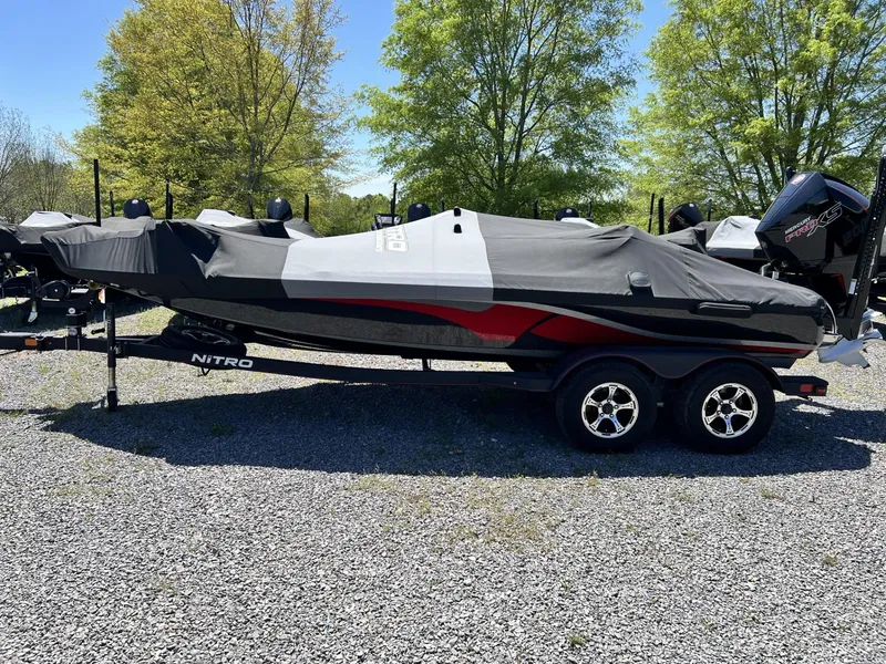 Slide: The Image of 2024 Nitro Z19 boat with cover on trailer, parked on gravel, surrounded by trees. - 4