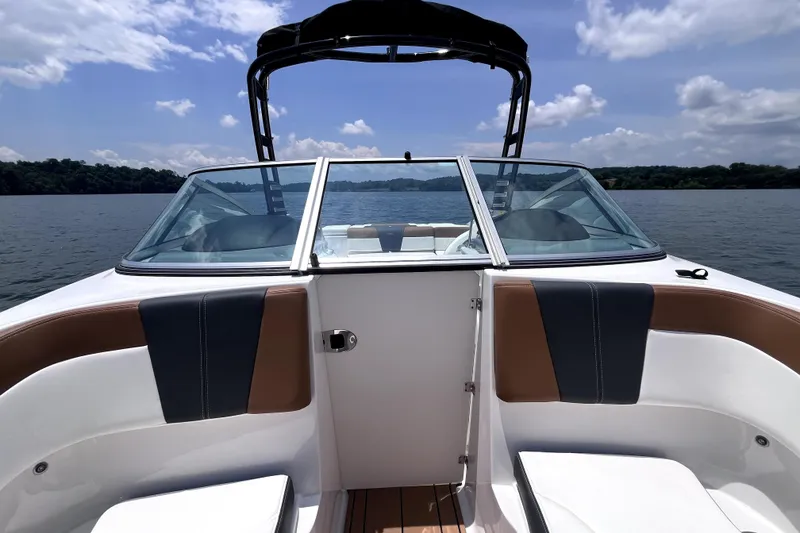 Slide: The Image of 2025 Chaparral 230 SSi boat interior with seating, on a lake under a blue sky. - 8