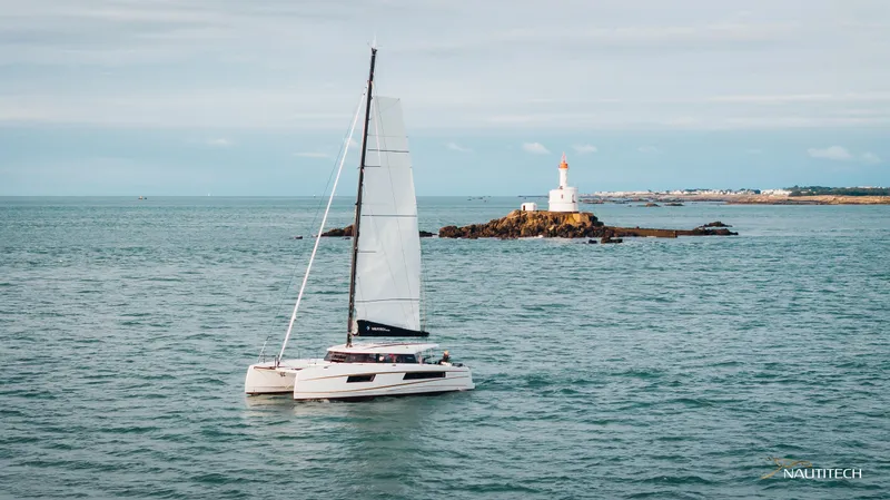 Slide: The Image of Sailing catamaran Nautitech 48 Open 2025 near a lighthouse on calm sea. - 0