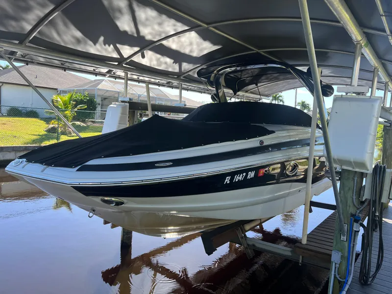 The Image of 2018 Crownline E26 XS boat on lift under canopy, docked by waterfront homes. - 0