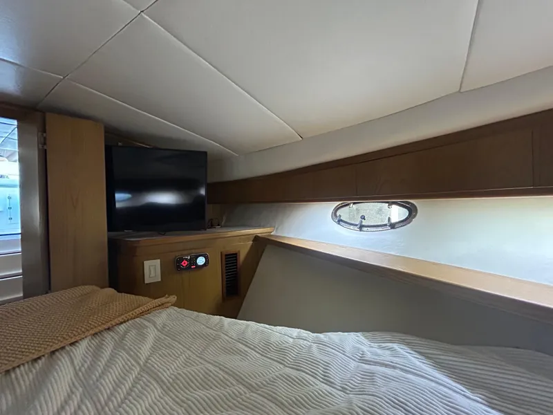 Slide: The Image of 1998 Tiara Yachts 3500 Express cabin interior with bed, TV, and porthole window. - 49