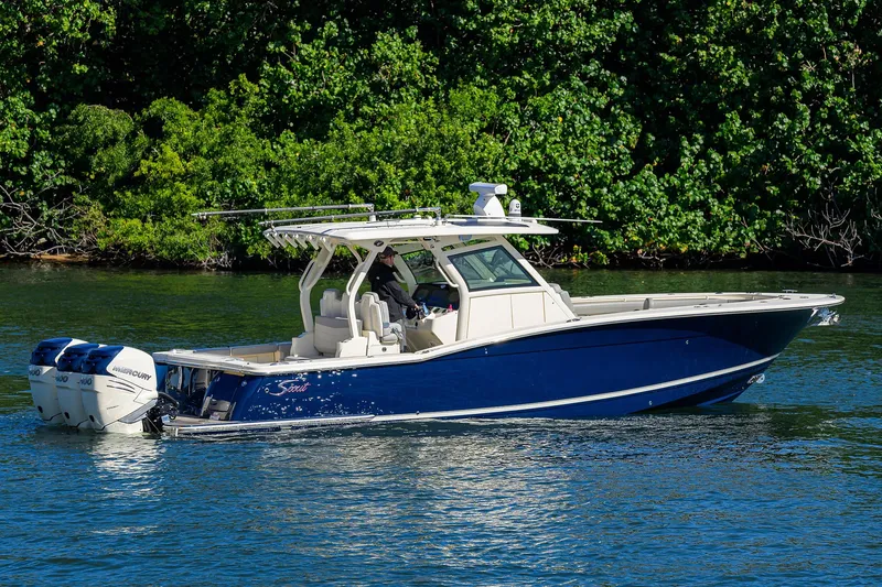 Slide: The Image of 2023 Scout 355 LXF boat on water, blue hull, lush green background. - 11