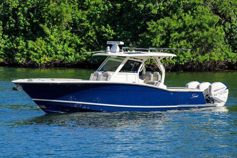 Slide: The Image of 2023 Scout 355 LXF boat cruising on a serene waterway with lush greenery. - 5