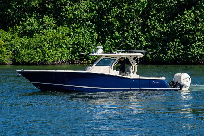 Slide: The Image of 2023 Scout 355 LXF boat cruising on a serene waterway with lush greenery. - 6