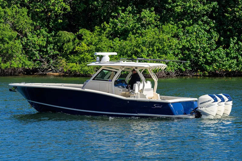 Slide: The Image of 2023 Scout 355 LXF boat cruising on a serene lake with lush green background. - 7