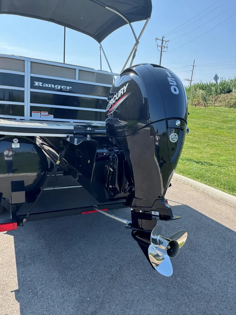 Slide: The Image of 2024 Ranger Reata 223C boat with Mercury 150 outboard motor, parked on pavement. - 2