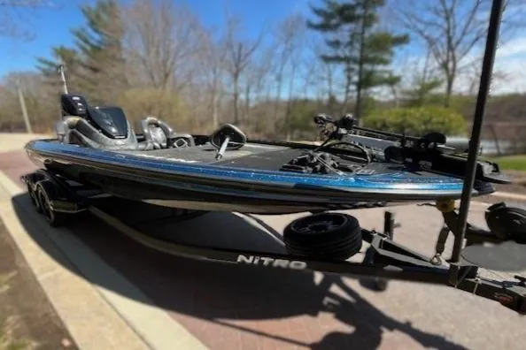 Slide: The Image of 2018 Nitro Z21 bass boat on trailer, parked outdoors with trees in background. - 4